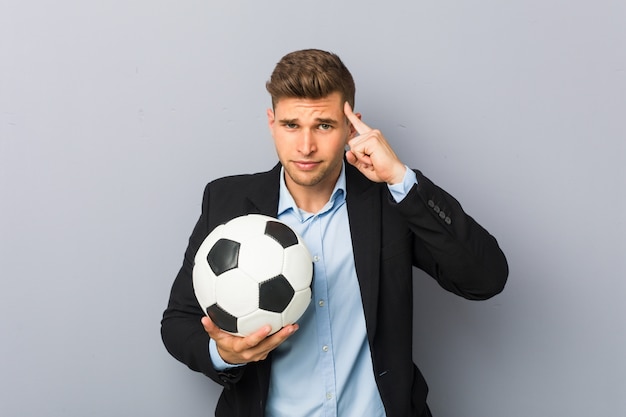 Jeune entraîneur de football pointant sa tempe avec le doigt, pensant, concentré sur une tâche.