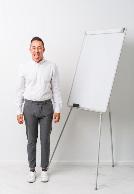 Jeune entraîneur homme avec un tableau blanc isolé drôle et sympathique qui sort la langue