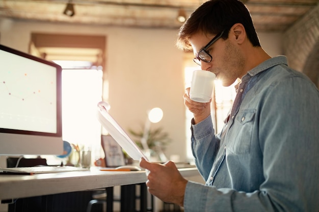 Jeune entrepreneur buvant du café et lisant des plans d'affaires au bureau