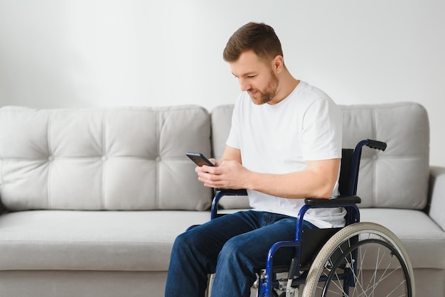 Jeune entrepreneur heureux en fauteuil roulant lisant un message sur un téléphone intelligent à la maison