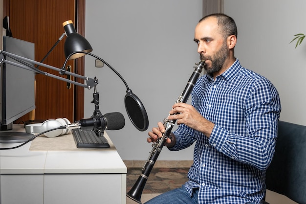 Jeune entrepreneur jouant de la clarinette à la maison et enregistrant de la musique pour la diffuser en ligne avec son ordinateur