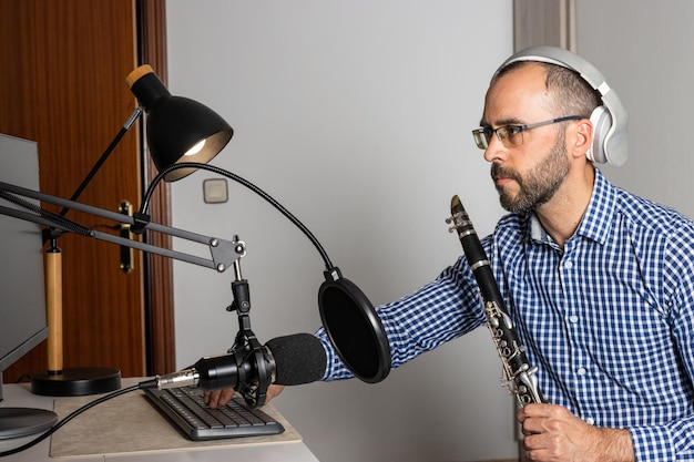 Jeune entrepreneur jouant de la clarinette à la maison et enregistrant de la musique pour la diffuser en ligne avec son ordinateur