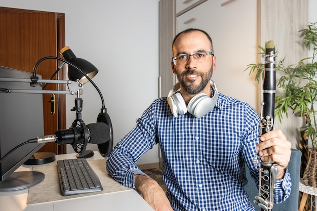 Jeune entrepreneur jouant de la clarinette à la maison et enregistrant de la musique pour la diffuser en ligne avec son ordinateur