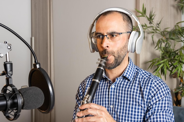 Jeune entrepreneur jouant de la clarinette à la maison et enregistrant de la musique pour la diffuser en ligne avec son ordinateur