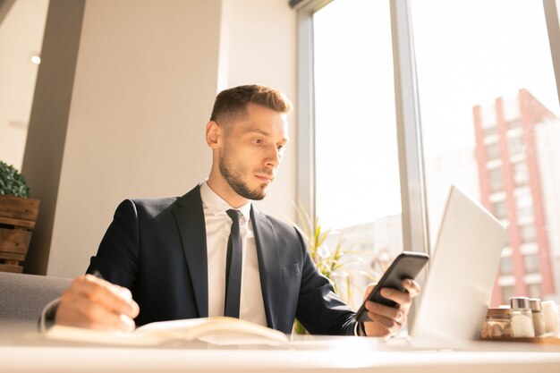 Jeune entrepreneur sérieux se concentrant sur le défilement dans le smartphone tout en regardant les rappels de rendez-vous