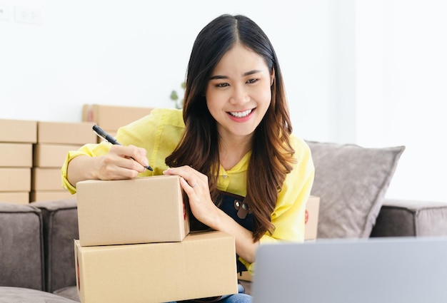 Un jeune entrepreneur souriant écrivant une adresse sur des boîtes de carton assis sur le canapé.