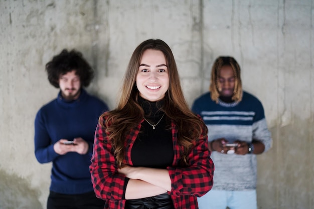 jeune équipe d'affaires décontractée multiethnique réussie utilisant des téléphones mobiles tout en se tenant devant un mur de béton au nouveau bureau de démarrage