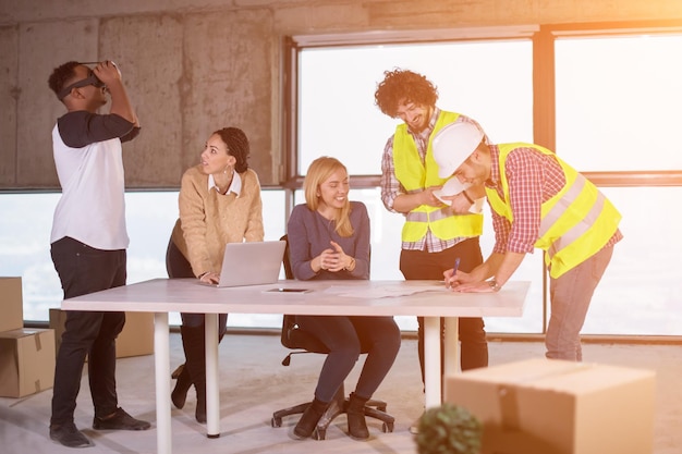 jeune équipe commerciale multiethnique vérifiant les documents et le flux de travail d'entreprise sur le chantier de construction à l'aide du casque de réalité virtuelle et de l'ordinateur portable avec la lumière du soleil à travers les fenêtres pendant le déplacement dans un