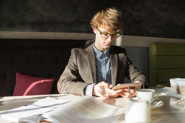 Jeune étudiant adolescent masculin moderne travaille avec tablet pc et livres sur une belle journée ensoleillée dans un restaurant confortable