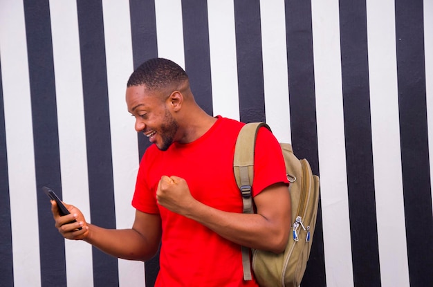 Jeune étudiant africain se sentant excité alors qu'il utilise son téléphone portable