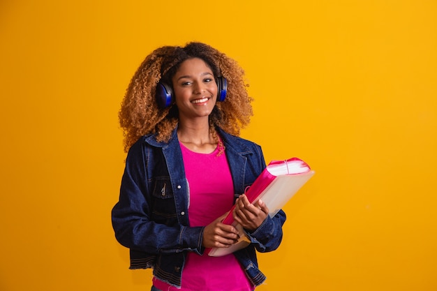 Jeune étudiant afro avec des livres sur fond jaune.