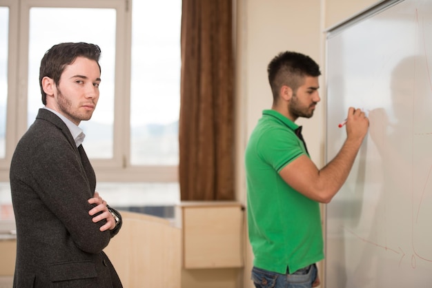 Un jeune étudiant arabe écrit une réponse sur le tableau blanc et le professeur l'observe