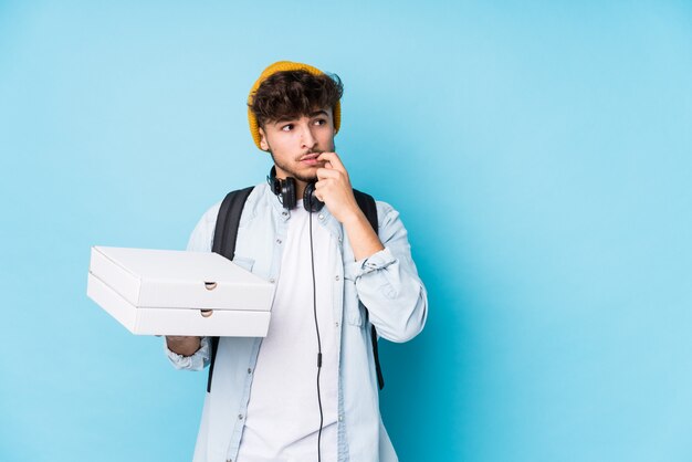 Jeune étudiant arabe homme tenant des pizzas isolées détendu penser à quelque chose en regardant un espace de copie.