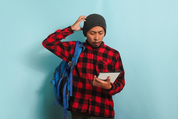 Un jeune étudiant asiatique surpris semble mécontent de sa main sur sa tête isolée sur fond bleu