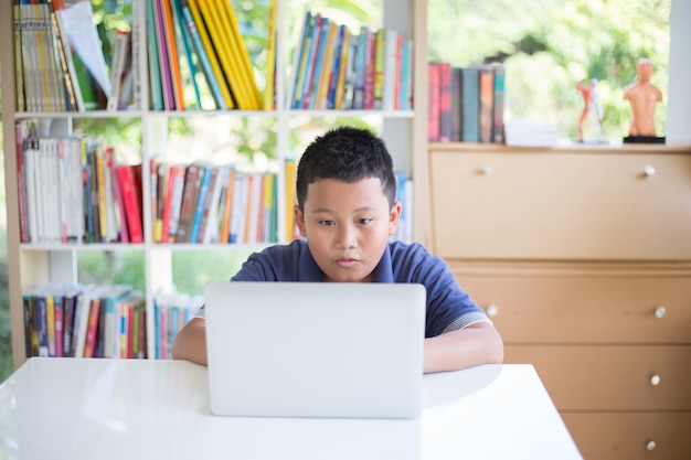 Jeune étudiant asiatique utilisant un ordinateur portable pour faire ses devoirs et apprendre à la bibliothèque de l&#39;école