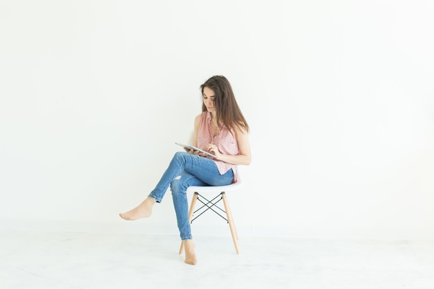 Jeune étudiant assis sur une chaise et à l'aide d'une tablette sur un mur blanc avec copie espace