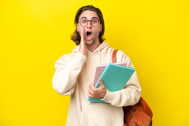 Jeune étudiant bel homme isolé sur fond jaune avec une expression faciale surprise et choquée