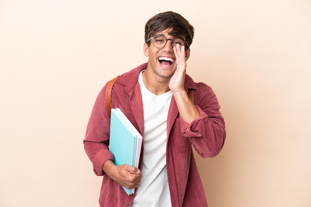 Jeune étudiant caucasien homme isolé sur fond ocre criant avec la bouche grande ouverte