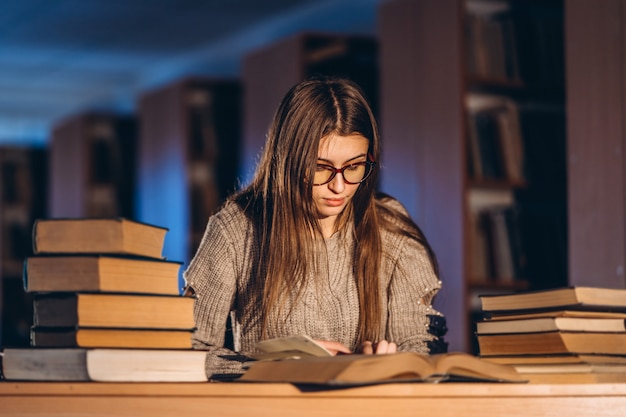 Jeune étudiant dans des verres se préparant à l'examen. Fille le soir est assise à une table dans la bibliothèque avec une pile de livres