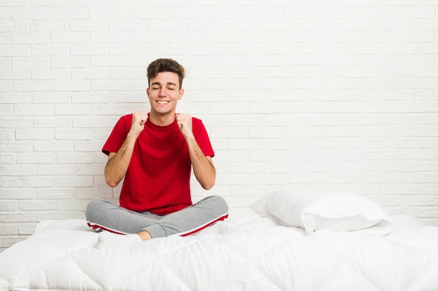 Jeune étudiant étudiant homme sur le lit en levant le poing, se sentir heureux et réussi. Concept de victoire.