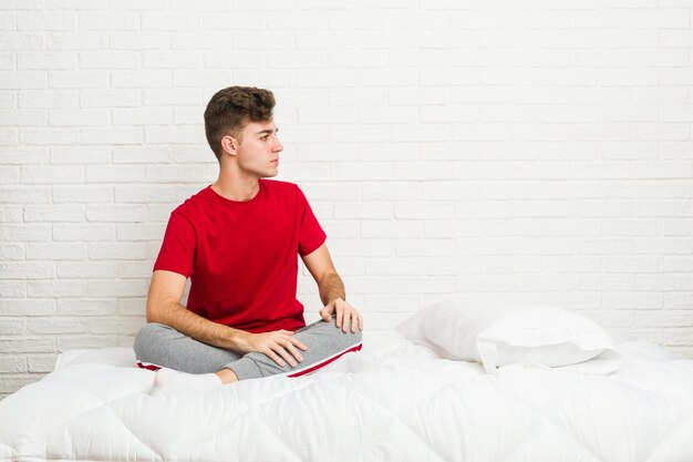 Jeune étudiant étudiant sur le lit, regardant à gauche, pose sur le côté.