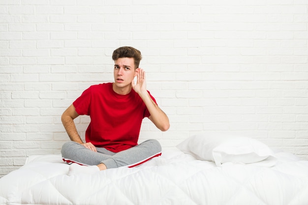 Jeune étudiant étudiant sur le lit en train d'écouter un commérage.