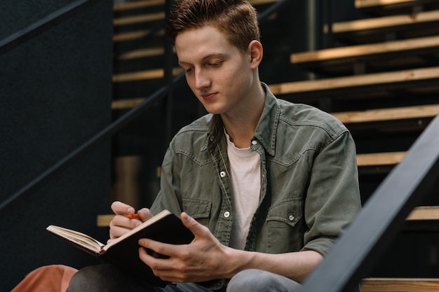 Jeune étudiant étudiant un livre de lecture prenant des notes Concept de l'éducation