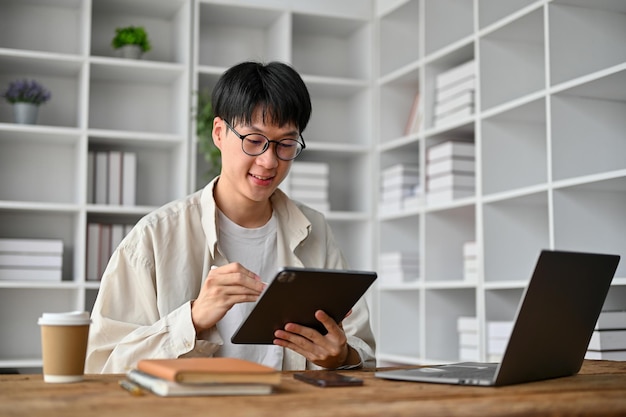 Jeune étudiant heureux avec des lunettes à l'aide d'une tablette dans la table d'étude