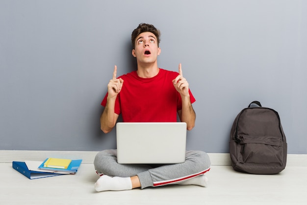 Jeune étudiant homme assis sur le sol de sa maison tenant un ordinateur portable