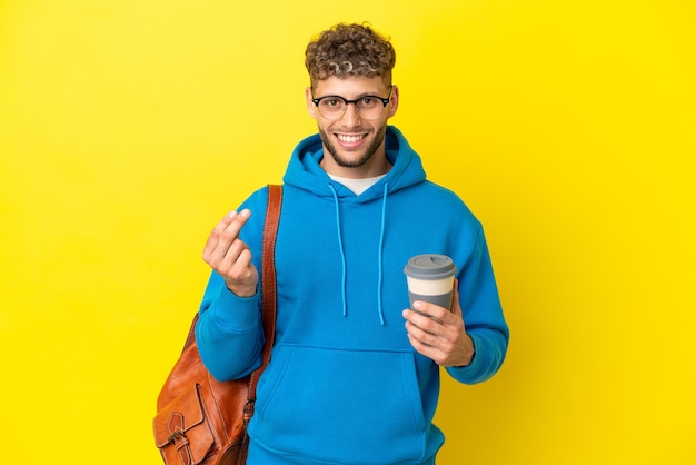 Jeune étudiant homme blond isolé sur fond jaune faisant un geste d'argent
