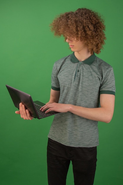 Un jeune étudiant en jeans avec un sac à dos tenant un ordinateur portable dans ses mains Isolé sur fond vert Étudier à l'université en ligne Communication vidéo Quarantaine