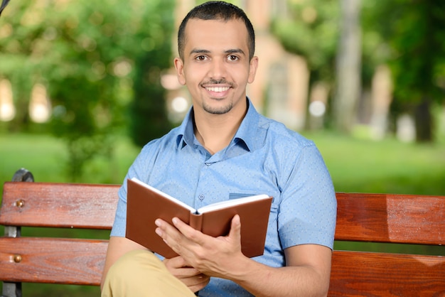 Jeune étudiant lisant un livre à l'extérieur dans le parc