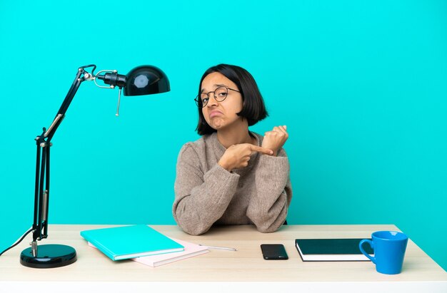 Jeune étudiant métisse femme étudiant sur une table faisant le geste d'être en retard