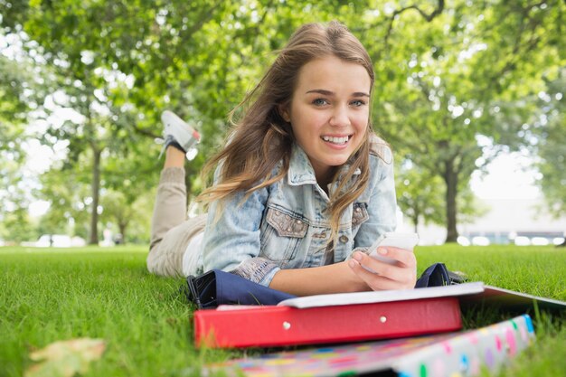 Jeune étudiant souriant couché sur l&#39;herbe en envoyant un texte