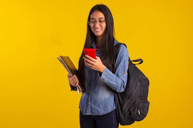 Jeune étudiant tenant des livres de sac à dos et regardant un téléphone portable en studio photo