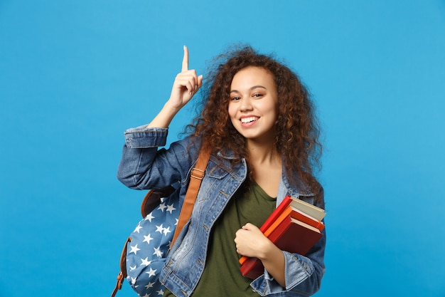 Jeune étudiant en vêtements en jean et sac à dos tient des livres isolés sur un mur bleu