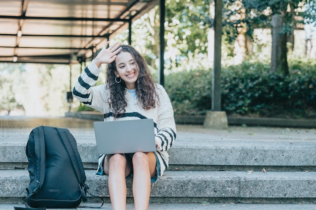 Jeune étudiante africaine ayant un appel vidéo sur un ordinateur portable sur le campus, souriant et montrant des choses à l'écran tout en s'amusant pendant l'échange.Contact avec la famille via internet.Connexion.