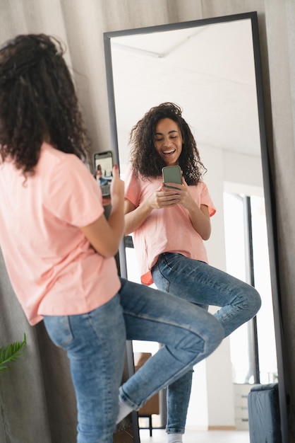 Une jeune étudiante africaine romantique se fait un selfie en regardant le miroir à la maison en se préparant pour un rendez-vous en bloguant en vlogging pour les médias sociaux en ligne