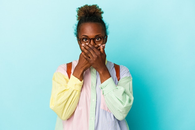 Jeune étudiante afro-américaine sur fond isolé choqué couvrant la bouche avec les mains.