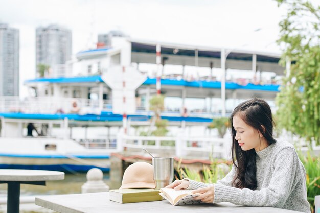 Jeune étudiante asiatique assis à table sur le campus et lire un livre pour se préparer aux examens