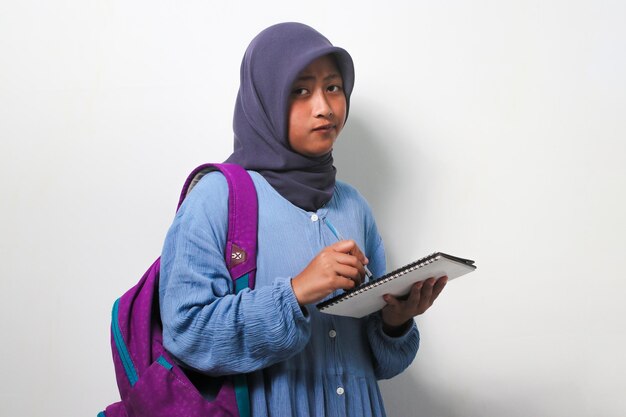 Jeune étudiante asiatique en hijab écrivant quelque chose sur le livre isolé sur fond blanc