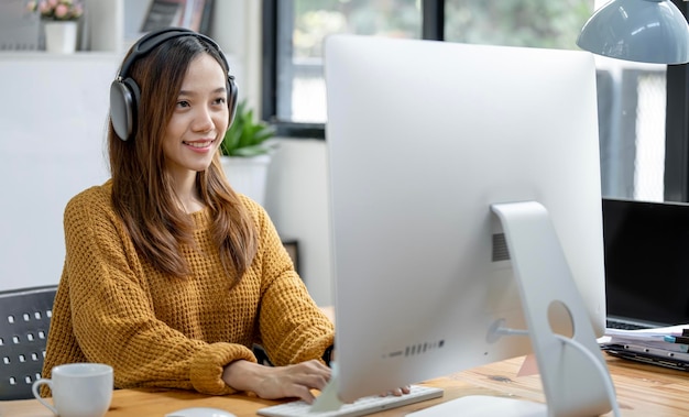 Jeune étudiante asiatique portant un casque travaillant et étudiant à domicile à l'aide d'un ordinateur de bureau