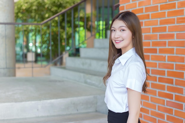 Une jeune étudiante asiatique sourit confiante et regarde la caméra en arrière-plan universitaire