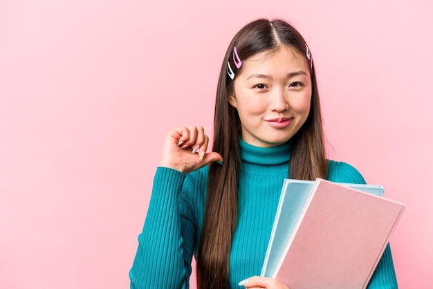 Jeune étudiante asiatique tenant des livres isolés sur fond rose se sent fière et confiante exemple à suivre