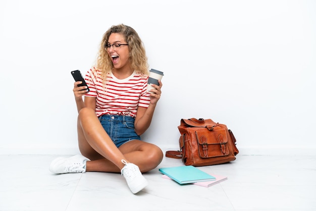 Jeune étudiante assise sur le sol tenant un café à emporter et un mobile