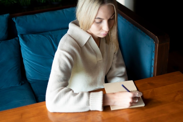 Une jeune étudiante assise à la table et écrivant dans un cahier