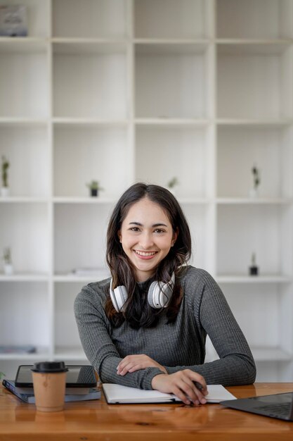 Une jeune étudiante avec un casque assis à la table en souriant et en regardant la caméra