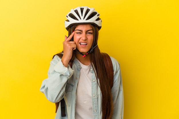 Jeune étudiante caucasienne portant un casque de vélo isolé sur fond jaune montrant un geste de déception avec l'index.