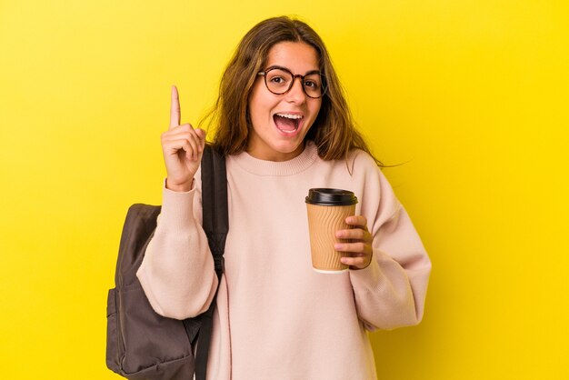 Jeune étudiante caucasienne tenant un café isolé sur fond jaune ayant une idée, un concept d'inspiration.