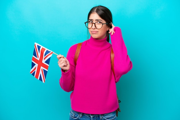 Jeune étudiante caucasienne tenant un drapeau anglais isolé sur fond bleu ayant des doutes